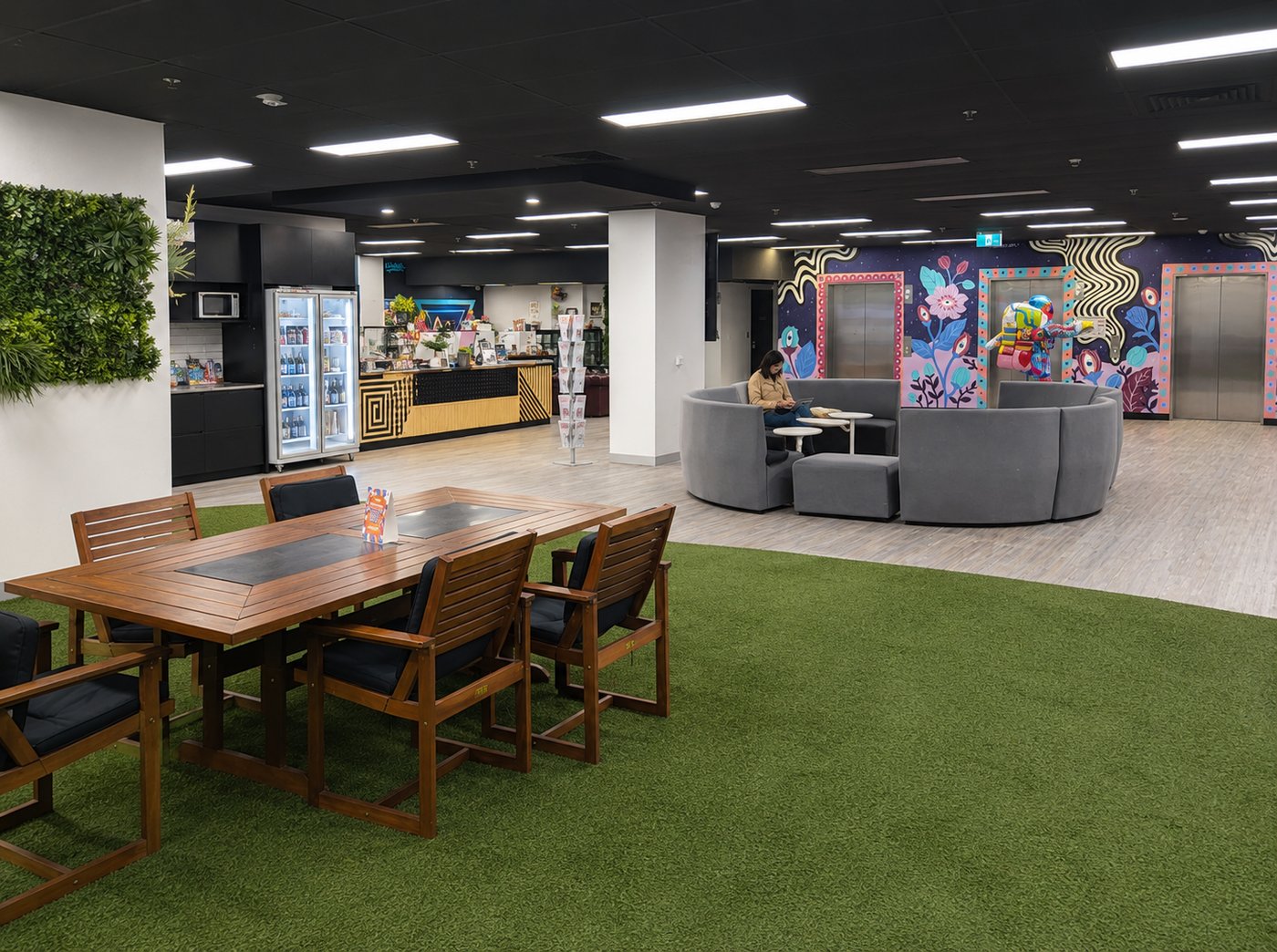 Shared breakout area with kitchenette, circular lounge seating and a colourful mural near the lift lobby