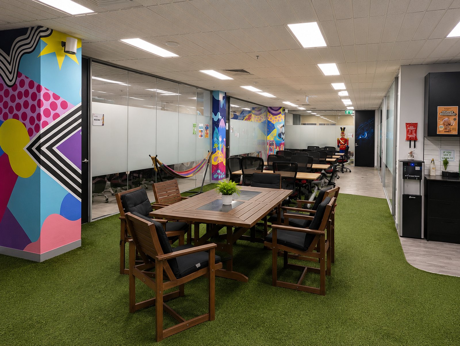 Common area with communal wooden table, artificial turf flooring and a colourful mural